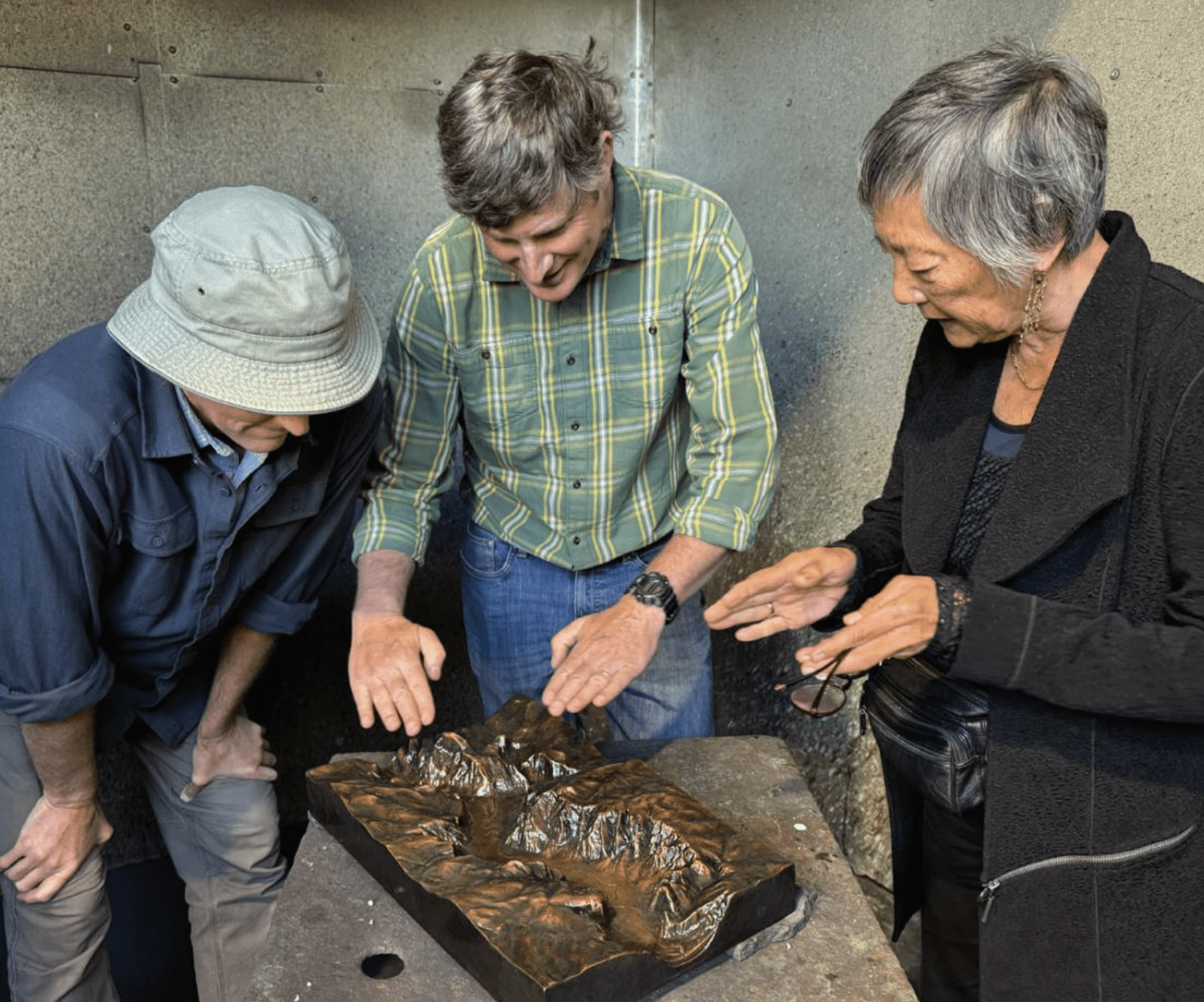 Three individuals admire a small, 3D brass replica of Tenaya Canyon.